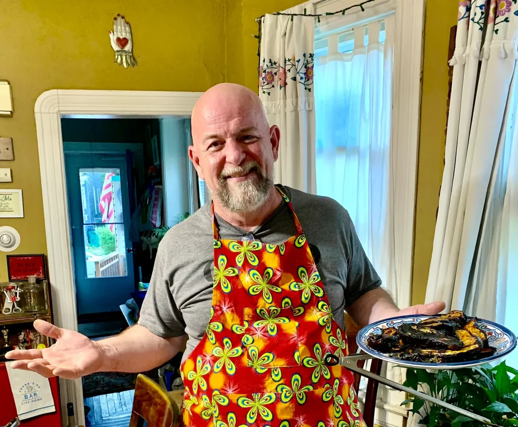 Andrew Galarneau, wearing apron custom-designed by his middle kid Will, holding a plate of grilled gochujang-miso eggplant.